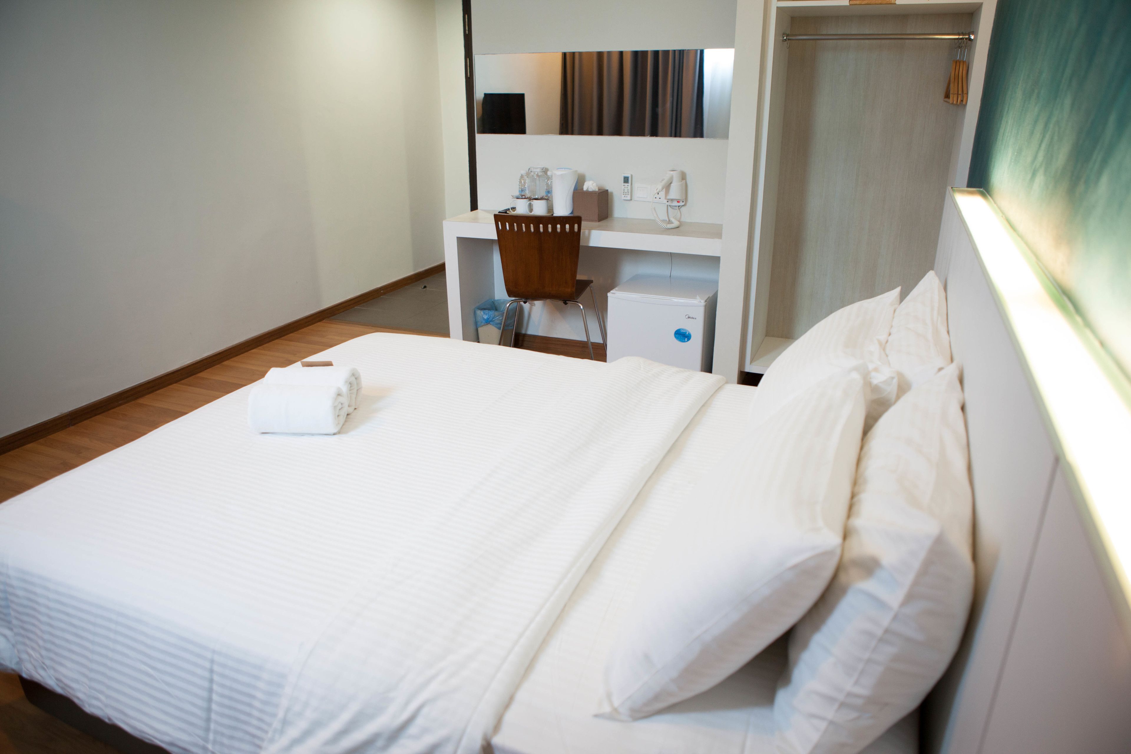 A hotel room with a neatly made bed, a desk with a chair, a small desk lamp, and a mirror.