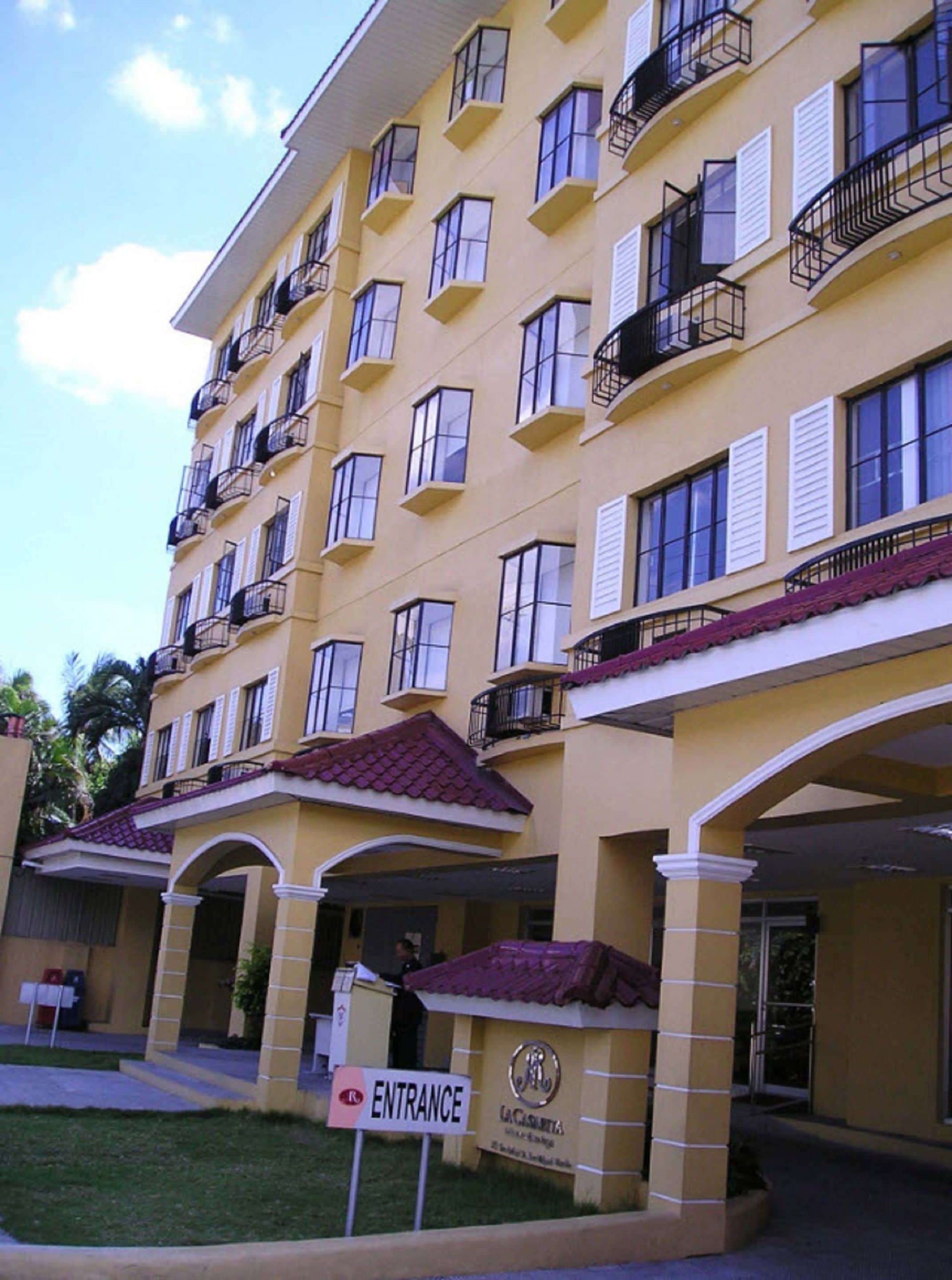 Un hôtel à plusieurs étages, avec une façade jaune, des balcons et une enseigne à l’entrée.