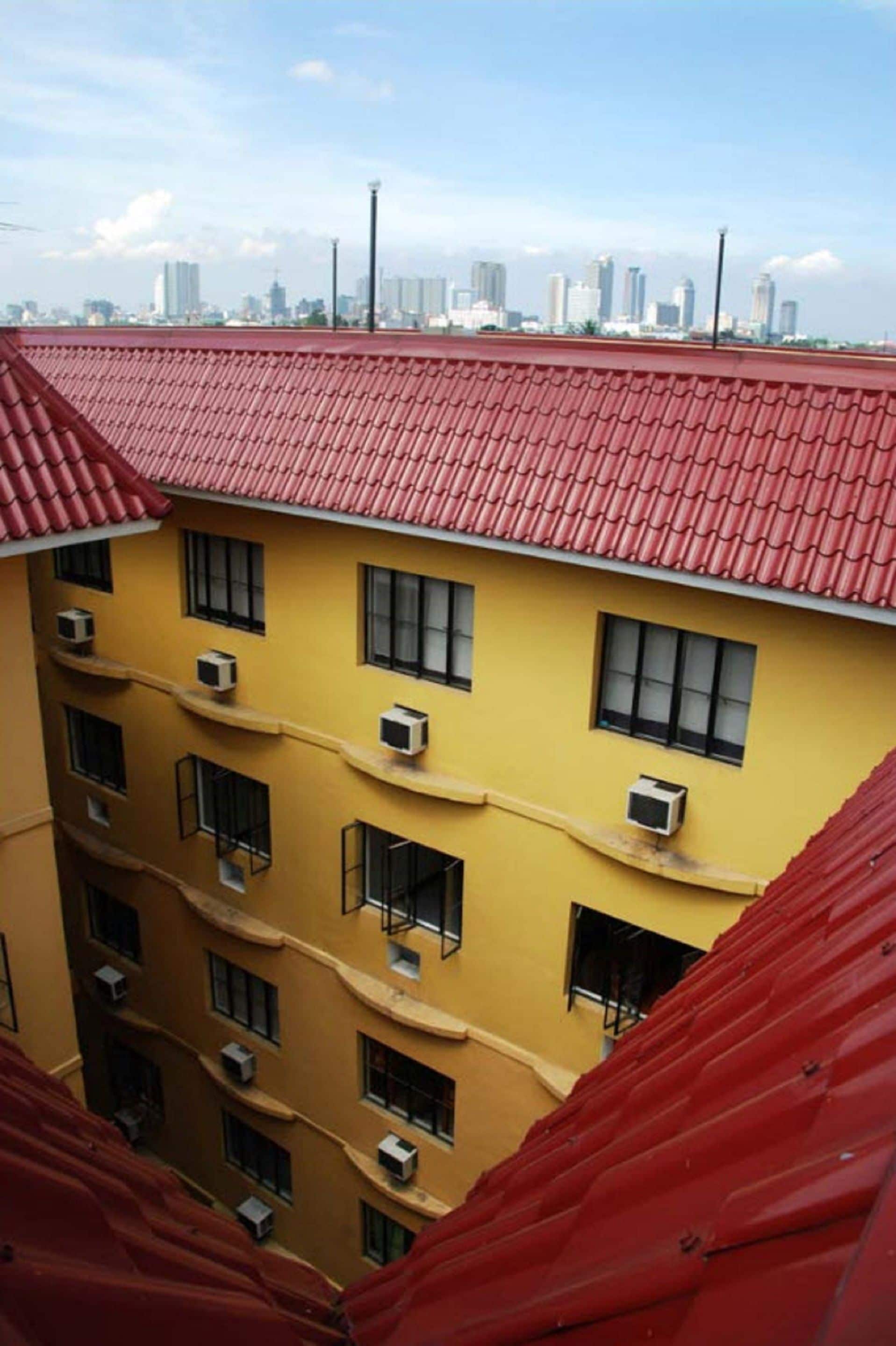 A multi-story building with a red roof and yellow walls, featuring multiple air conditioning units and windows.