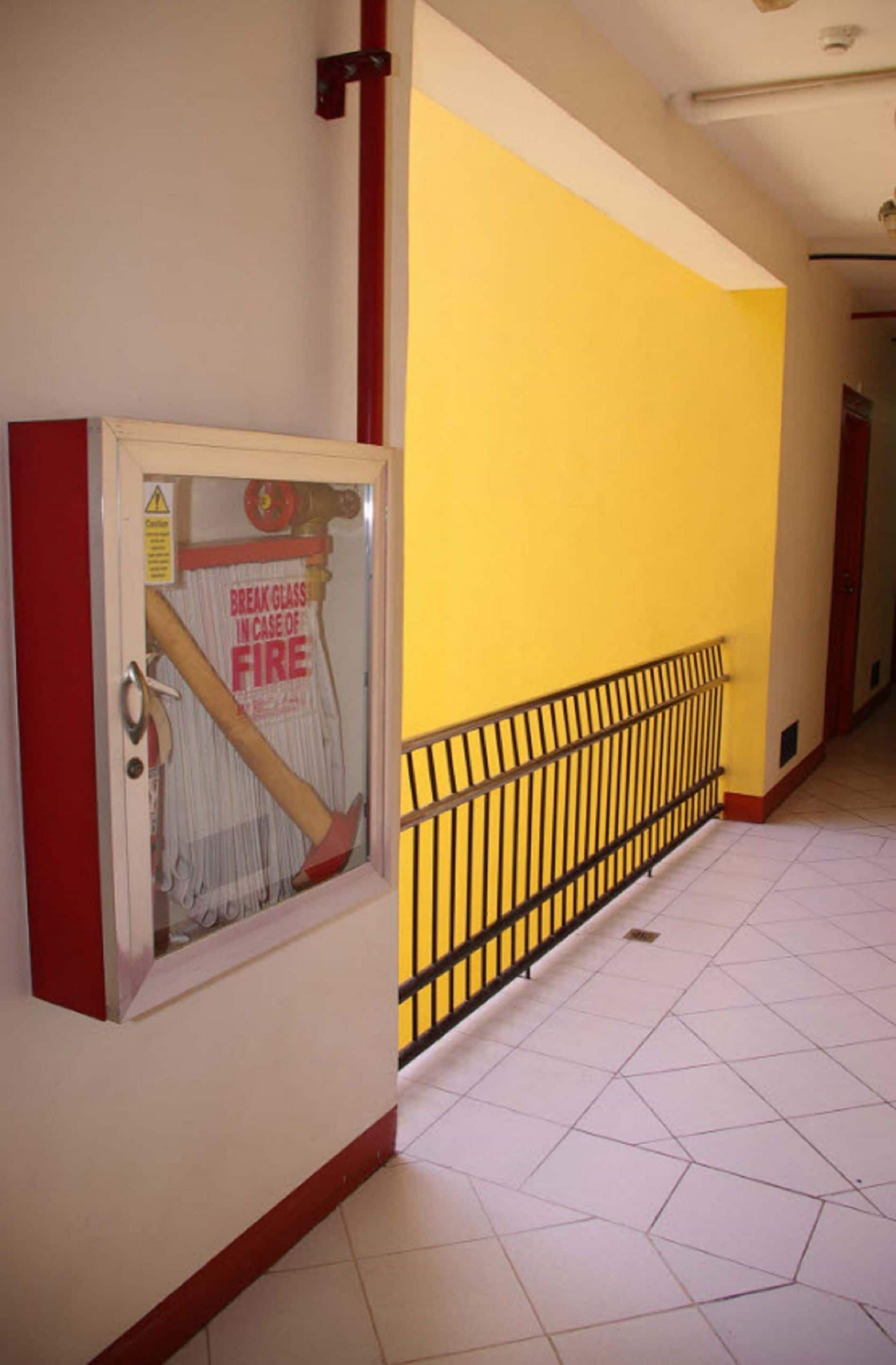 A hallway with yellow walls, a fire safety glass door, and a metal railing.