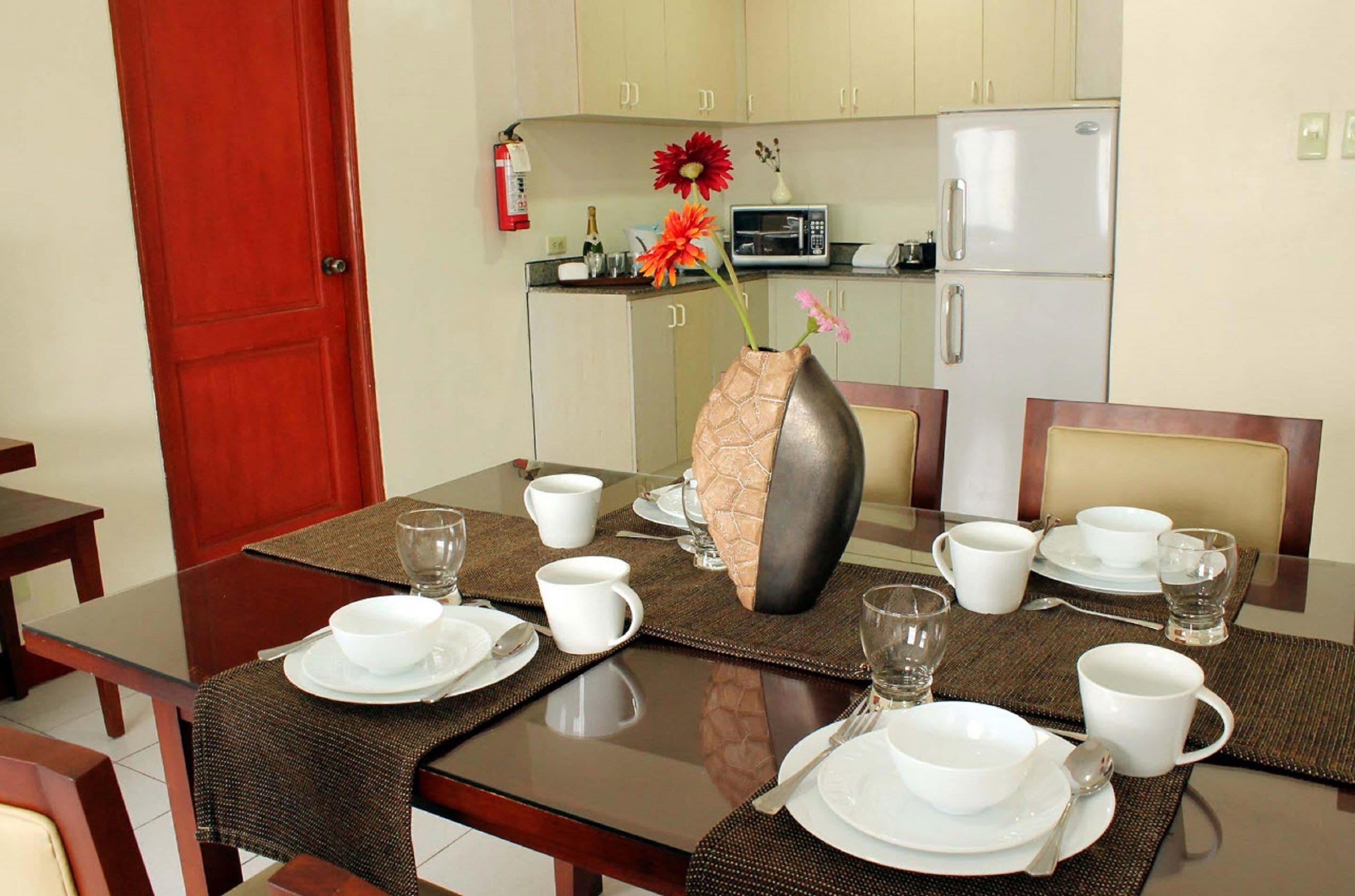 Uma mesa de jantar posta com pratos, tigelas e xícaras brancos, com um vaso de flores ao centro.