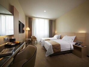 Habitación de hotel con dos camas, un escritorio, una silla, un televisor y una lámpara.