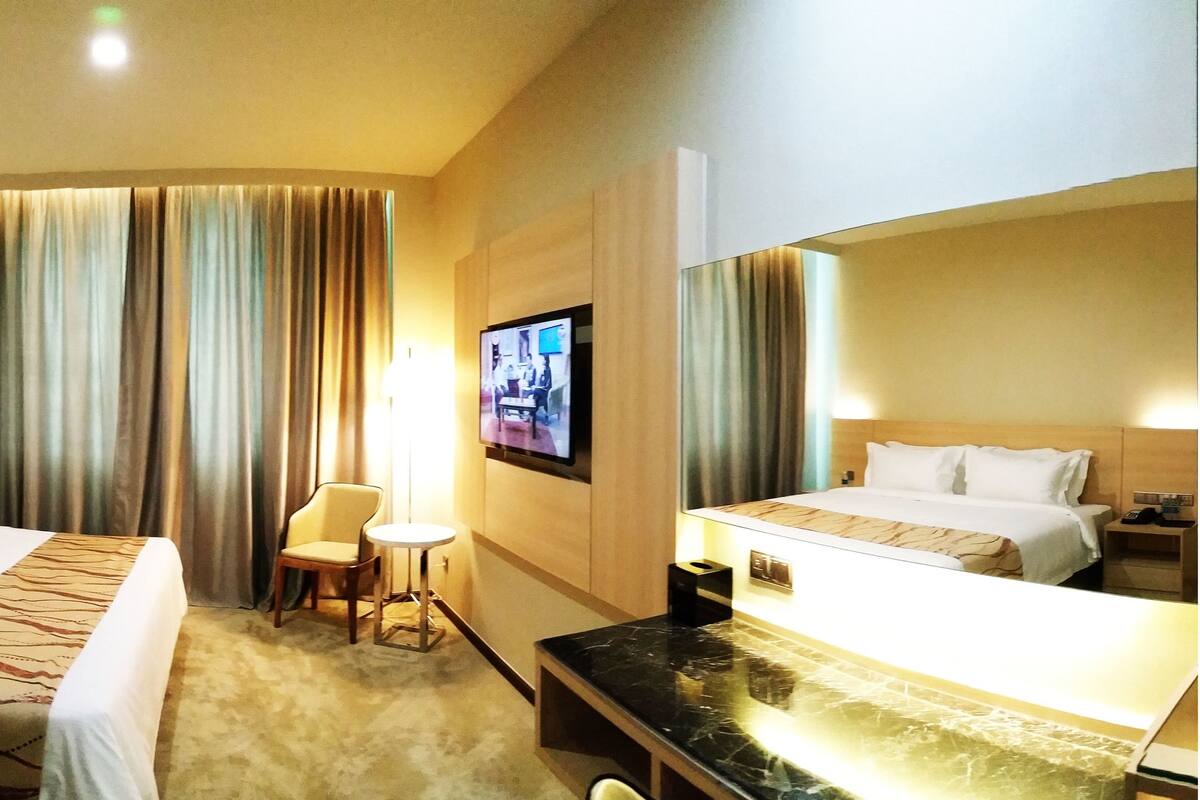 Una habitación de hotel con dos camas, una mesita, una silla, un televisor y un espejo.