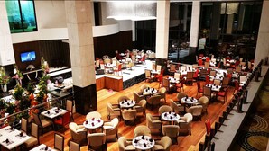 Un amplio vestíbulo de hotel con varias zonas de restauración, una recepción y una pantalla de televisión grande.