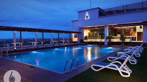 Área de piscina en la azotea con sillones de descanso, un bar y vistas a la ciudad.