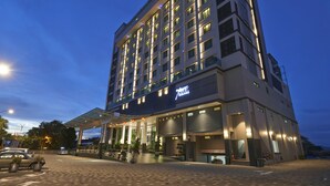 Un hotel de varios pisos con diseño moderno, que destaca por una entrada imponente con marquesina de vidrio y un letrero con el nombre del hotel.