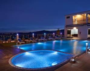 Un área de piscina en la azotea con sillones de descanso y un edificio moderno.