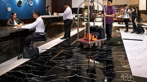 Vestíbulo de hotel con una mesa de recepción, un carrito de equipaje y un área de descanso.