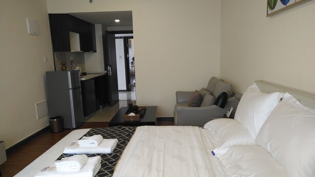 Quarto de hotel com cama, sofá, uma mesinha e uma cozinha compacta ao fundo.