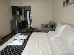 Een hotelkamer met een bed, een bank, een tafeltje en een kitchenette op de achtergrond.