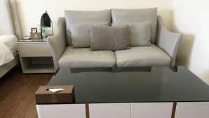 Uma sala de estar moderna com sofá, mesa de centro de vidro e mesa de cabeceira com abajur e controle remoto.