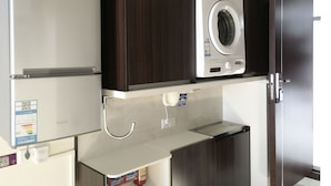 Uma cozinha compacta com máquina de lavar embutida, um frigorífico pequeno e um micro-ondas.