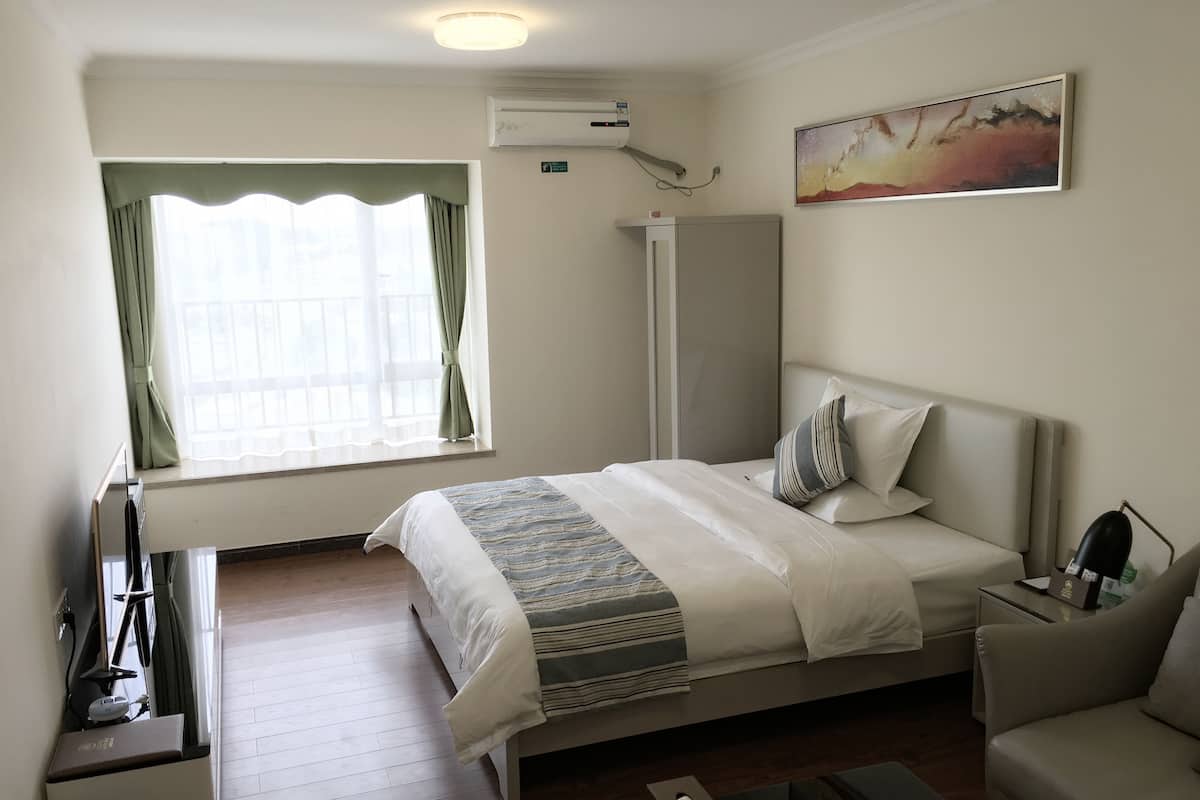 Une chambre d’hôtel avec un lit, un bureau, une chaise, une armoire et un tableau au mur.