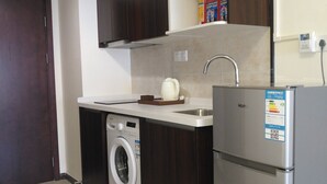 Cozinha compacta com armários de madeira escura, máquina de lavar embutida, geladeira de aço inoxidável e painel de azulejos.