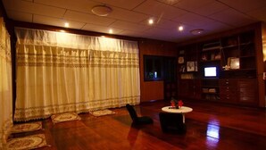 A room with a wooden floor, a black chair, a small round table with a vase, and a television on a wooden cabinet. - Chezmoi Handicraft & HomeStay (Chiang Rai)