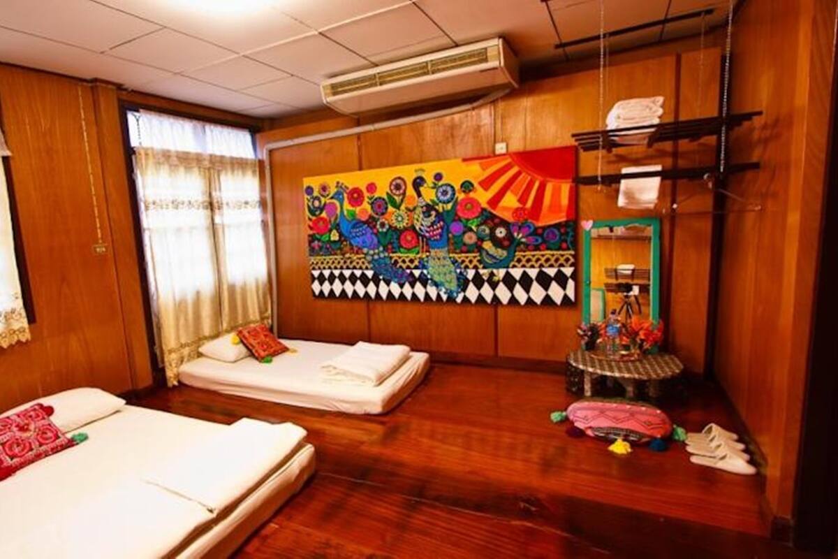 A room with two beds, wooden walls, a colorful mural, and a small table with a camera and flowers.