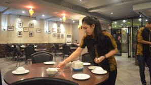 Une salle à manger avec des tables dressées pour le service, une femme qui sert les plats et un homme qui se tient à proximité.
