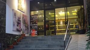 L’entrée d’un hôtel, avec un escalier, des plantes en pot et une affiche publicitaire pour un service de massage.