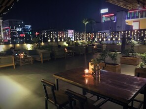 Un espacio al aire libre con mesas, sillas, luces colgantes y plantas en macetas.