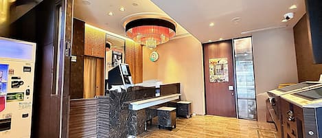 Un vestíbul d'hotel amb una taquilla d'admissió, una màquina expenedora, un rellotge i una porta.