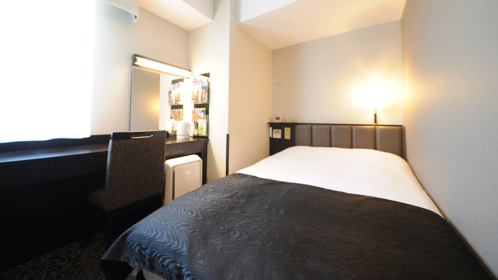 Camera d'albergo con un letto, una scrivania, una sedia, un tavolino, uno specchio e una lampada a parete.