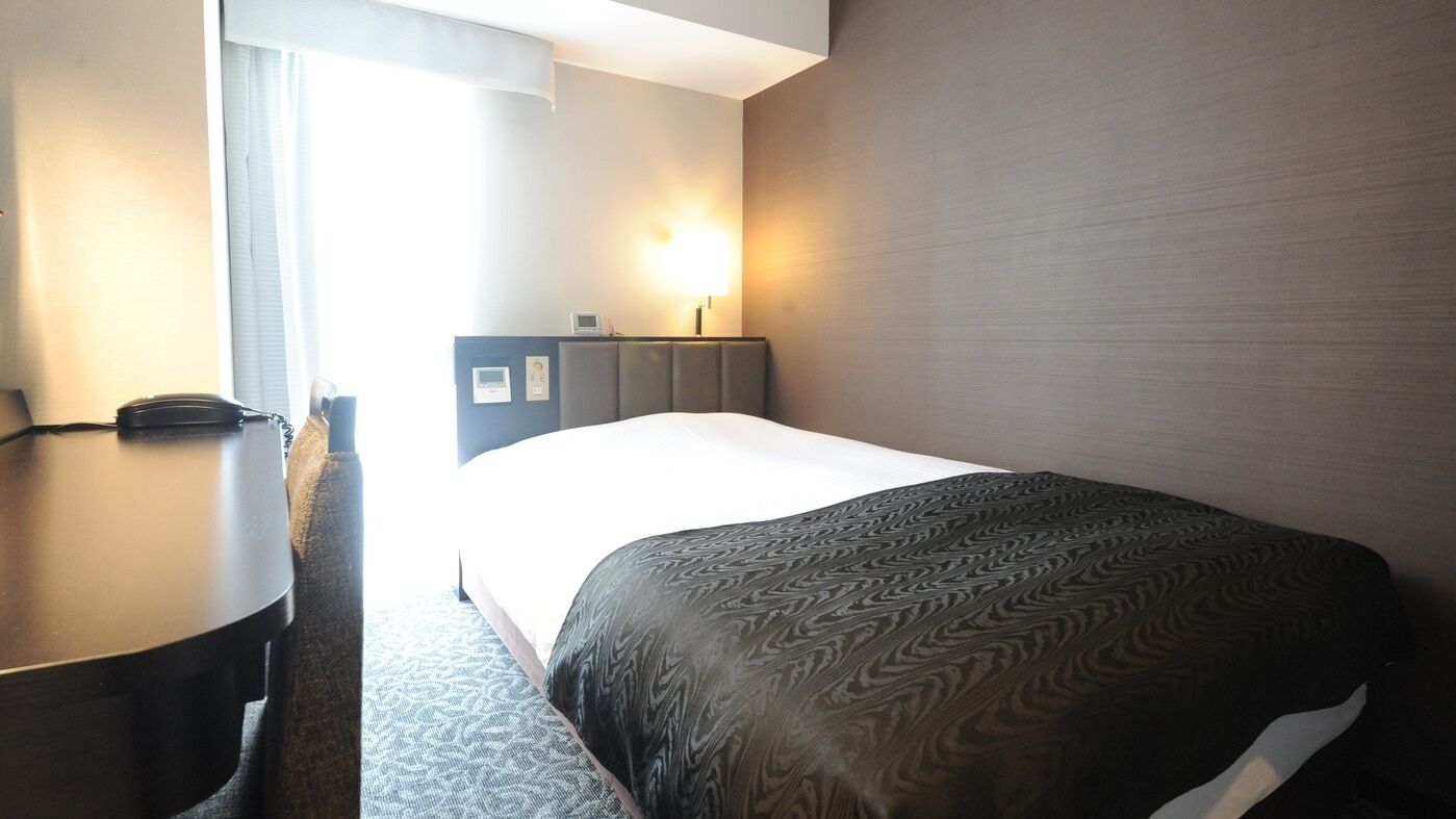 Una camera d'albergo con un letto, una scrivania, una lampada e una finestra.