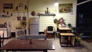 A kitchen with a refrigerator, a fan, a table, and a chair. There are decorative items on the wall and a poster of ducks. - Milin Guesthouse (Chiang Rai)
