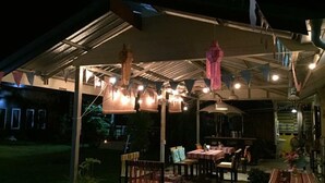 An outdoor patio area with tables and chairs, a covered seating area, and string lights. - Milin Guesthouse (Chiang Rai)