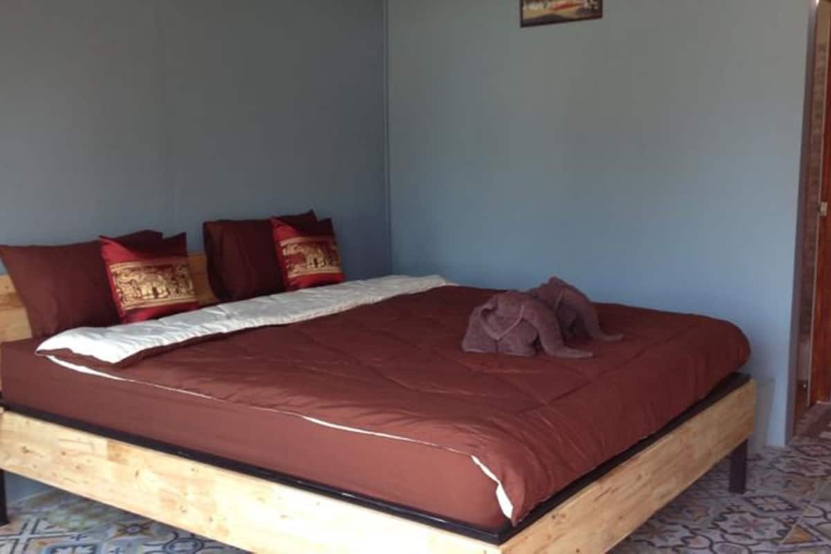 Quarto com estrutura de cama de madeira, colcha vermelha e várias almofadas.