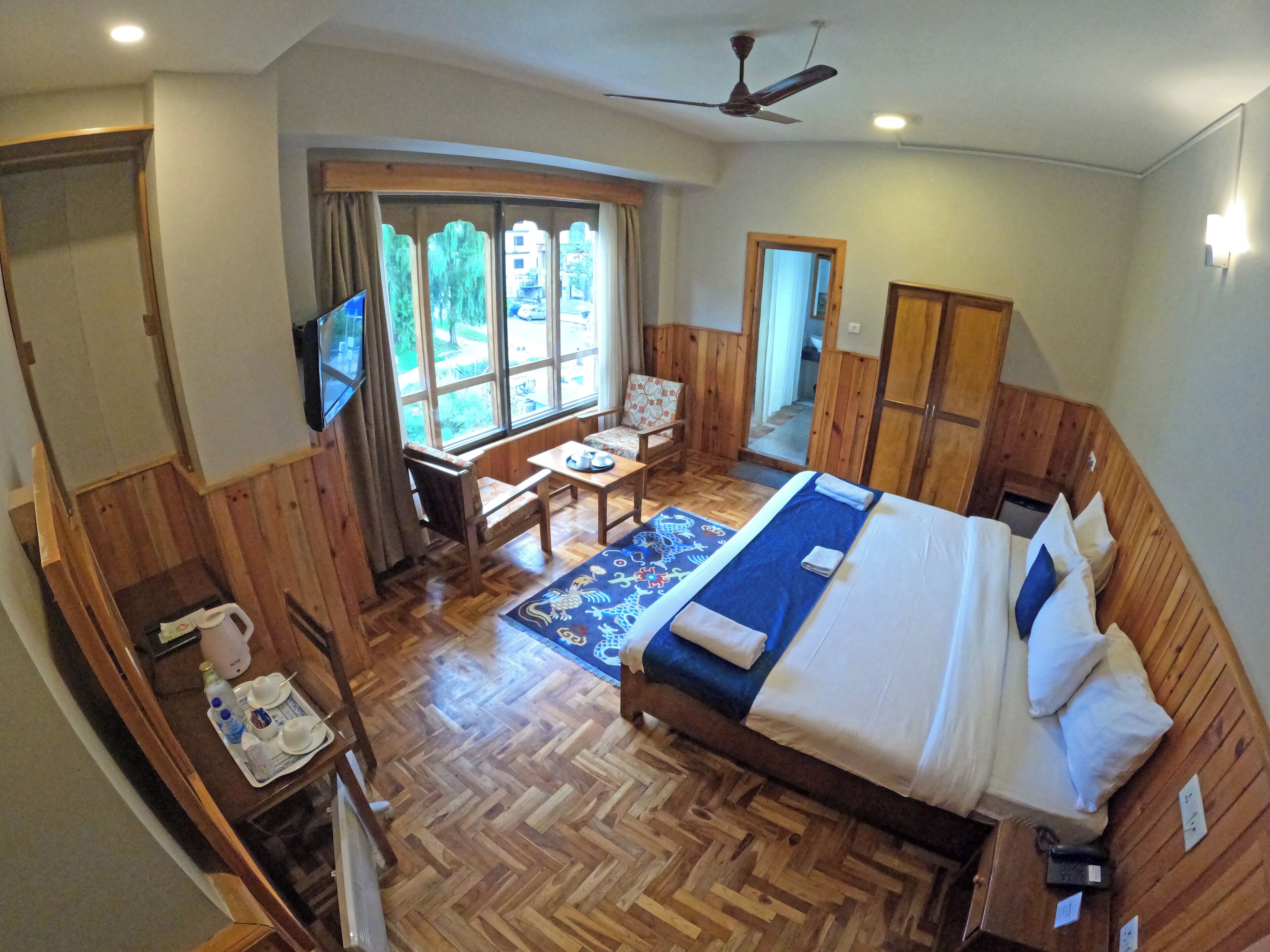 A hotel room with a bed, a desk, a chair, a TV, and a window with a view of the outside.