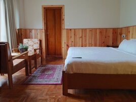 Una stanza con parete rivestita in legno, un letto con biancheria bianca, una scrivania in legno con una sedia e un tappeto decorativo sul pavimento.