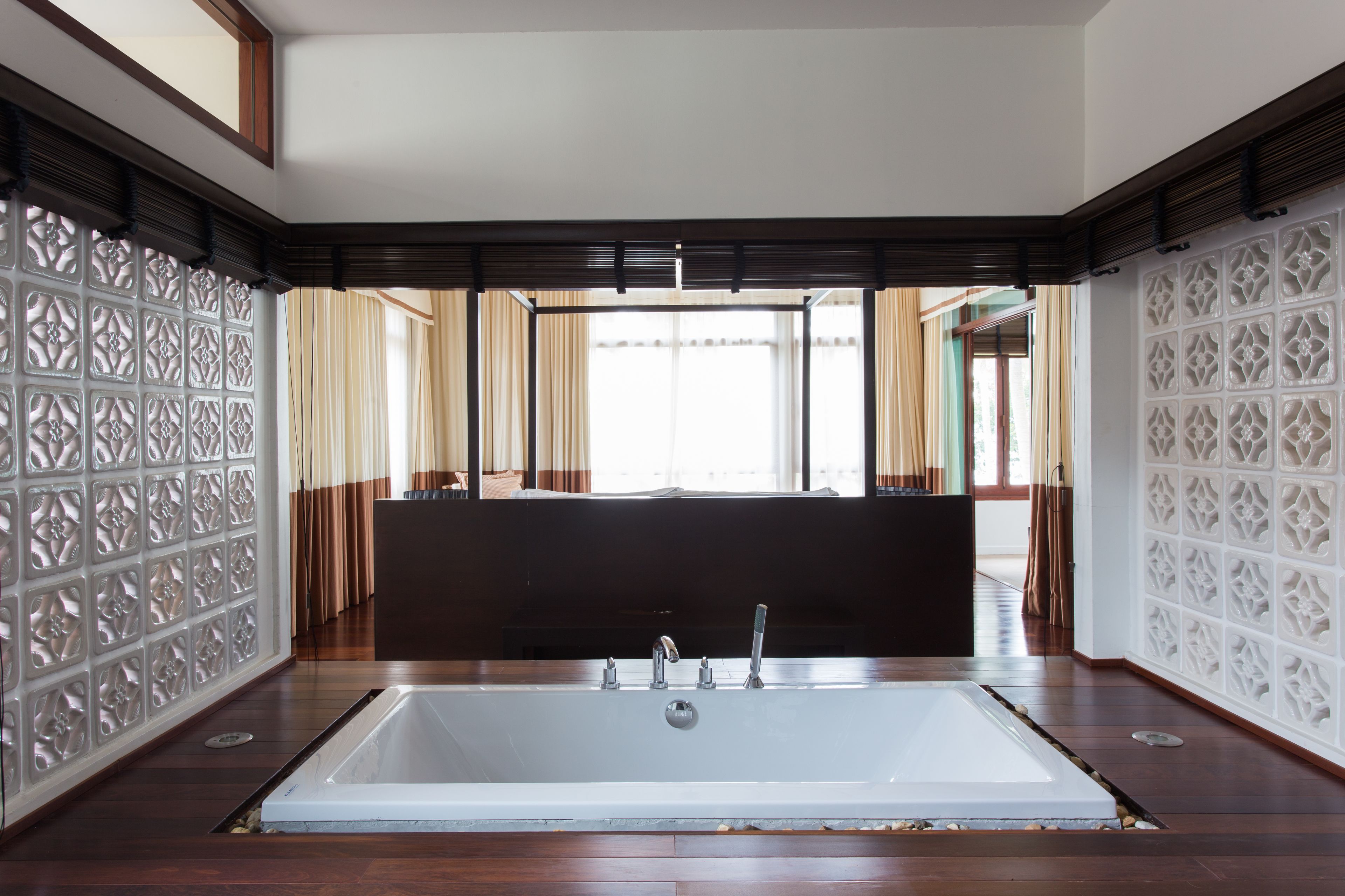Ein modernes Badezimmer mit einer großen Badewanne, Holzboden, dekorativen Wandverkleidungen und einem Ausblick ins Freie durch große Fenster.