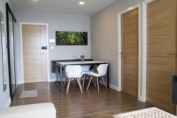 A modern room with a wooden floor, a dining table with chairs, a painting on the wall, and a closed door. - Establiss By Weena (Bangkok)