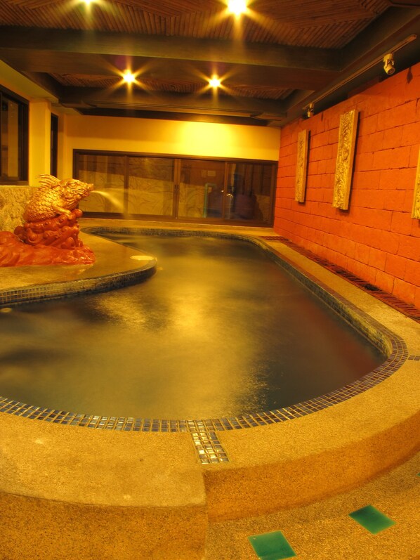 A hot tub with a decorative dragon statue, surrounded by a tiled floor and a brick wall.