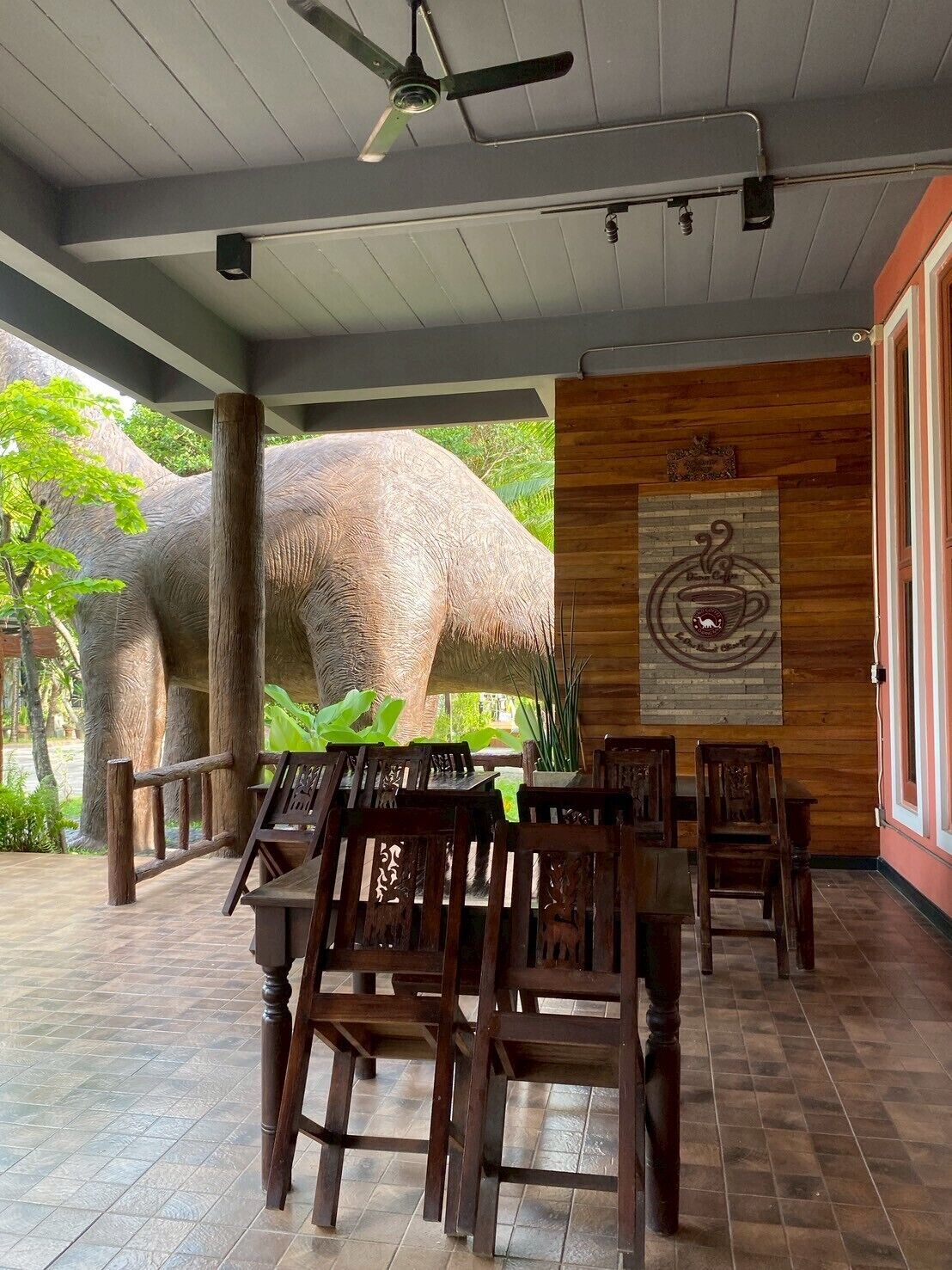 A covered outdoor seating area with wooden furniture and a large elephant sculpture.