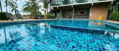 Una piscina con suelo de baldosas, rodeada de sillones de descanso y palmeras.