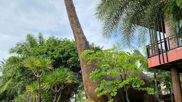 Una estatua de dinosaurio en un jardín exuberante con palmeras y un edificio al fondo.