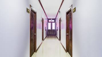 A long, narrow hallway with wooden doors on either side, leading to a room with a large window.