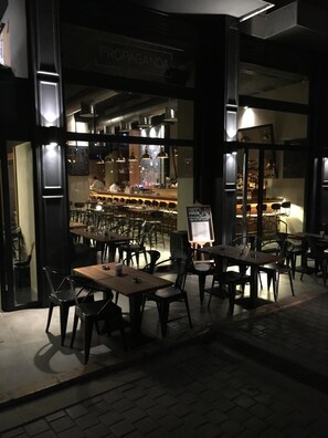 An outdoor seating area with tables and chairs, a bar in the background, and a sign that reads "PROPAGANDA".
