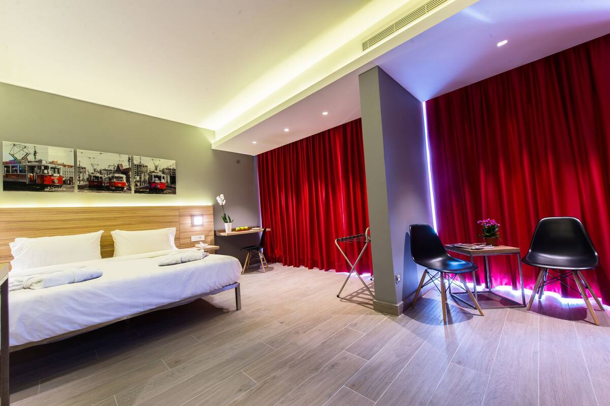Habitación de hotel con cama, escritorio, dos sillas y una cortina roja.
