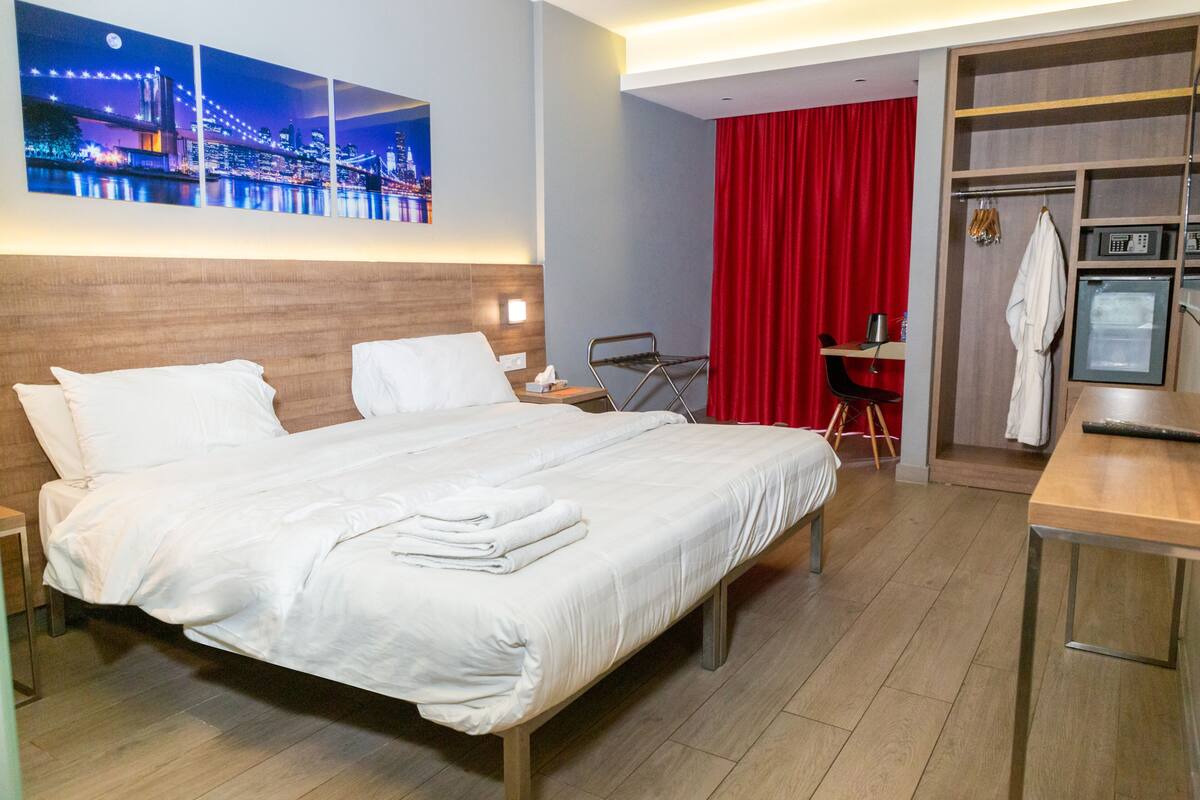 Una habitación de hotel con una cama grande, un escritorio con una silla, un microondas y una cortina roja.