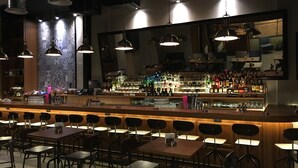 Zona de bar con mostrador, taburetes y luces colgantes.