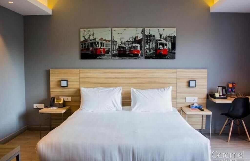Habitación de hotel con una cama grande, un escritorio con silla, un teléfono y una obra de arte en la pared que representa tranvías.