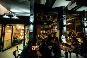 Um espaço de refeições interno lotado, com várias mesas e cadeiras, um quadro de menu visível e uma parede de tijolos.