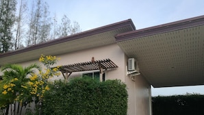 A building with a covered parking area, a pergola, and a well-maintained garden with yellow flowering plants and a large bush.