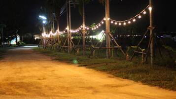 A dirt road at night with string lights and wooden structures.