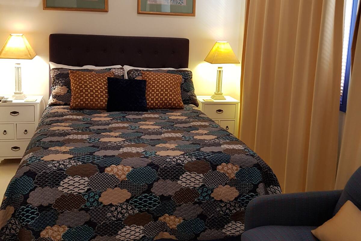 A neatly made bed with a patterned quilt, two bedside lamps, and two framed artworks on the wall.
