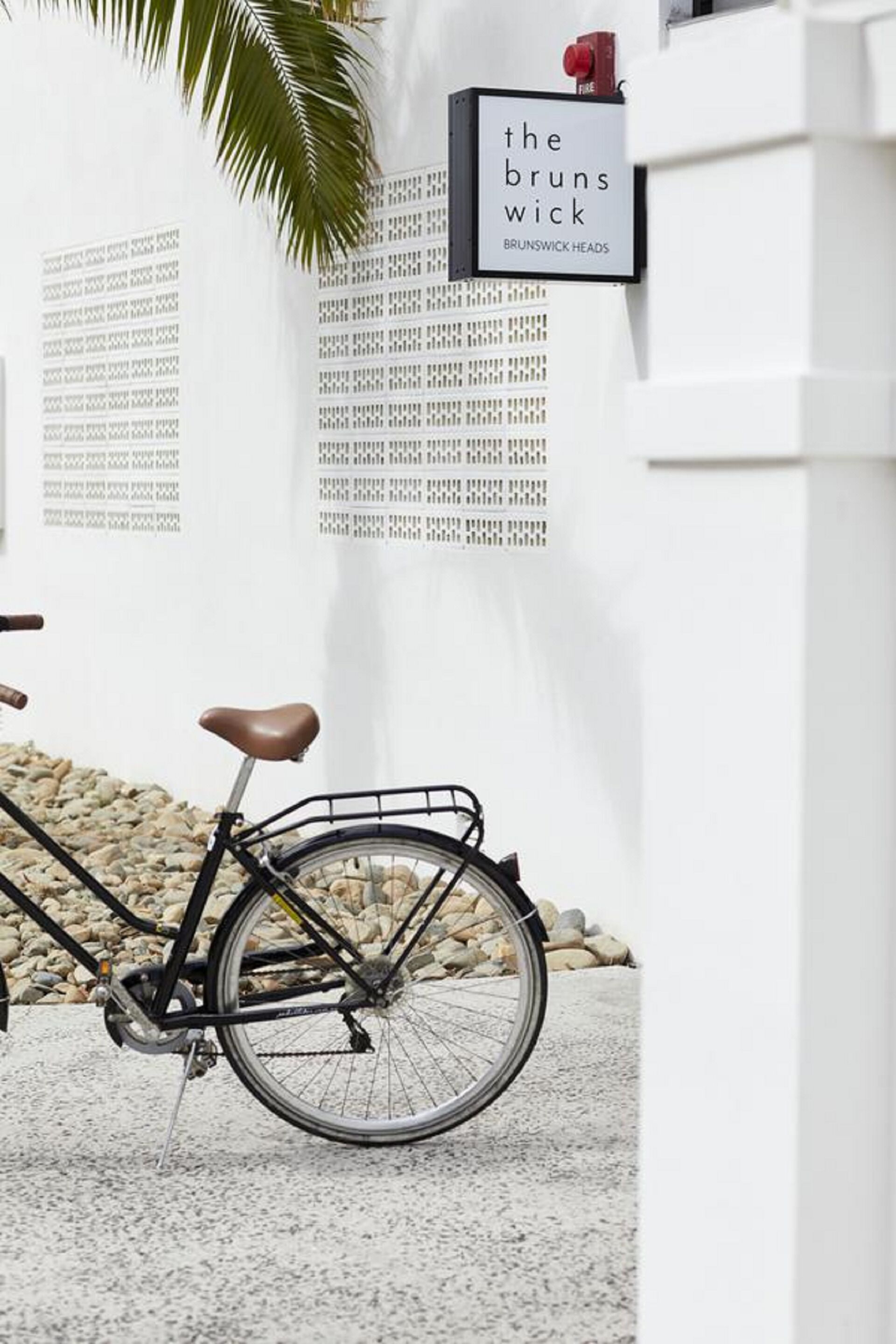 A bicycle parked in front of a wall with a sign reading "the brunswick" and "BRUNSWICK HEADS".
