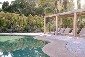 Zona de piscina amb gandules i una pèrgola de fusta.