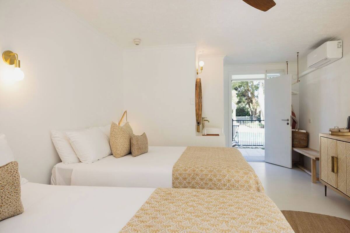 A hotel room with two beds, a wardrobe, a desk, and a view of the outdoors.